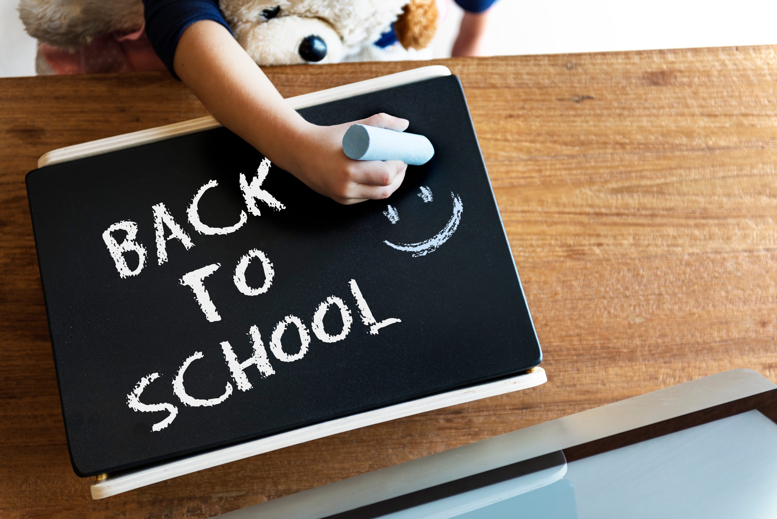 la mano di un bambino scrive su una lavagnetta nera la scritta "back to schoool"