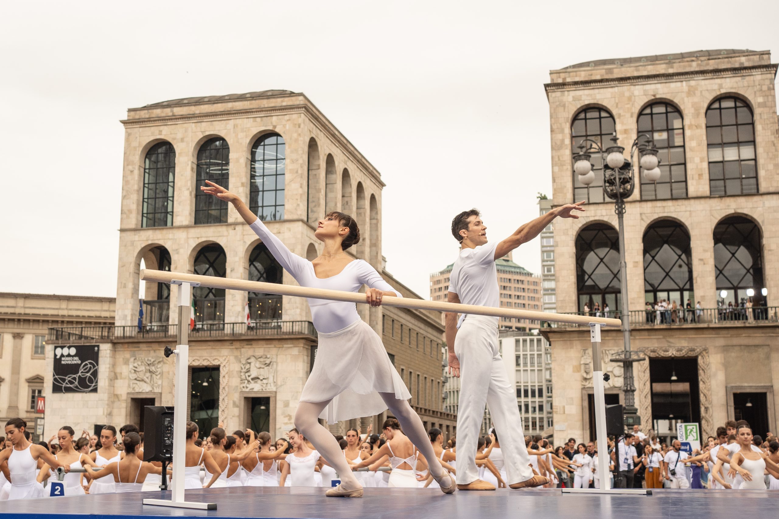 roberto bolle e nicoletta manni vestiti di bianco alla sbarra sullo sfondo il museo dei novecento di milano