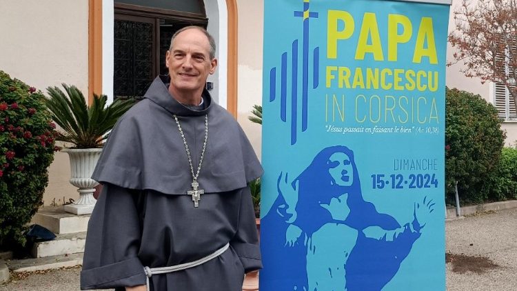 uomo vestito con saio di fianco a un manifesto blu